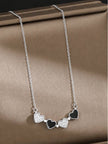 Four alternating CZ pavé and black enamel heart charms arranged in a row on a silver cable chain, laid flat on a taupe surface