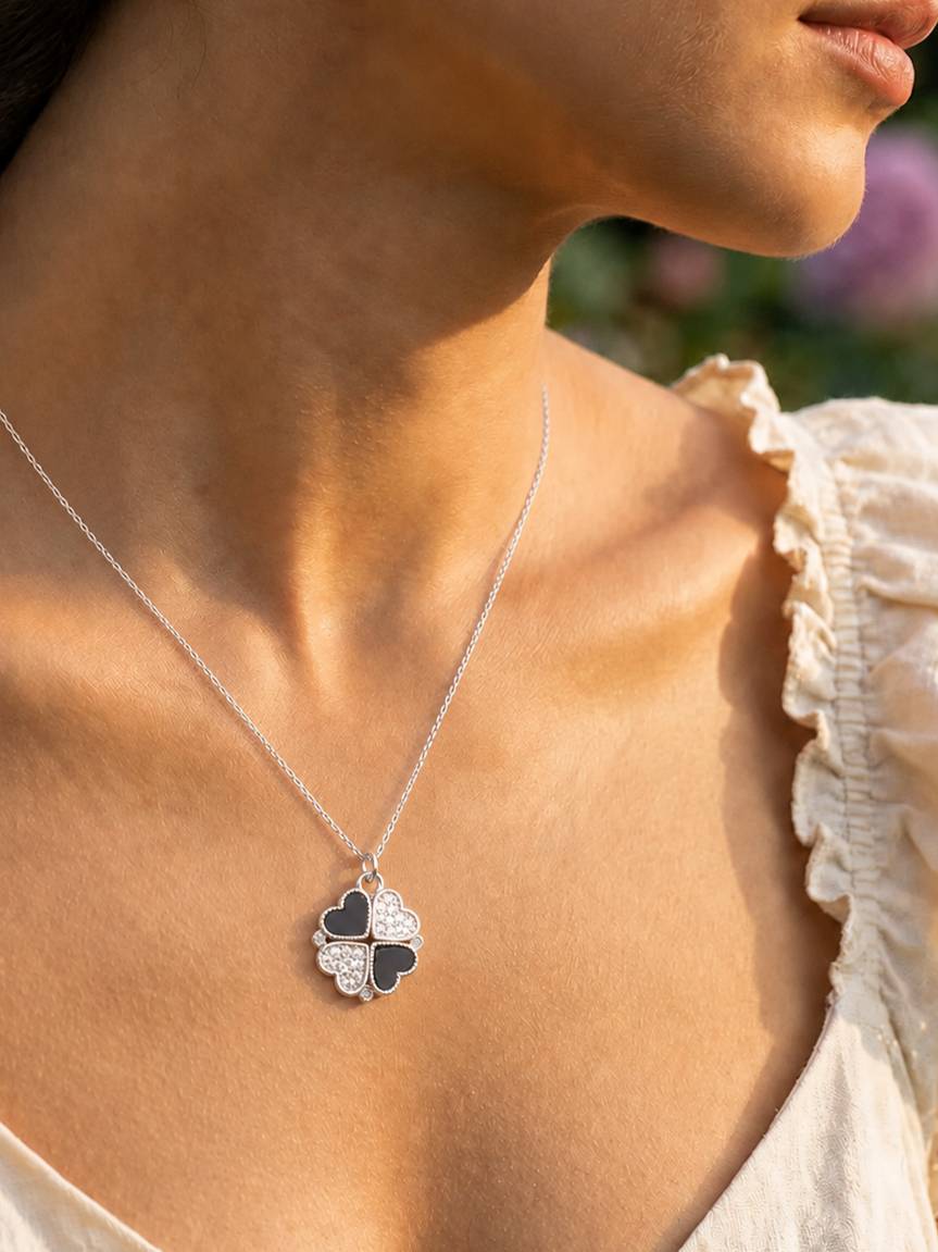 Close-up of the silver-tone clover pendant with two black enamel and two CZ hearts worn on a woman's neckline over a white ruffled top