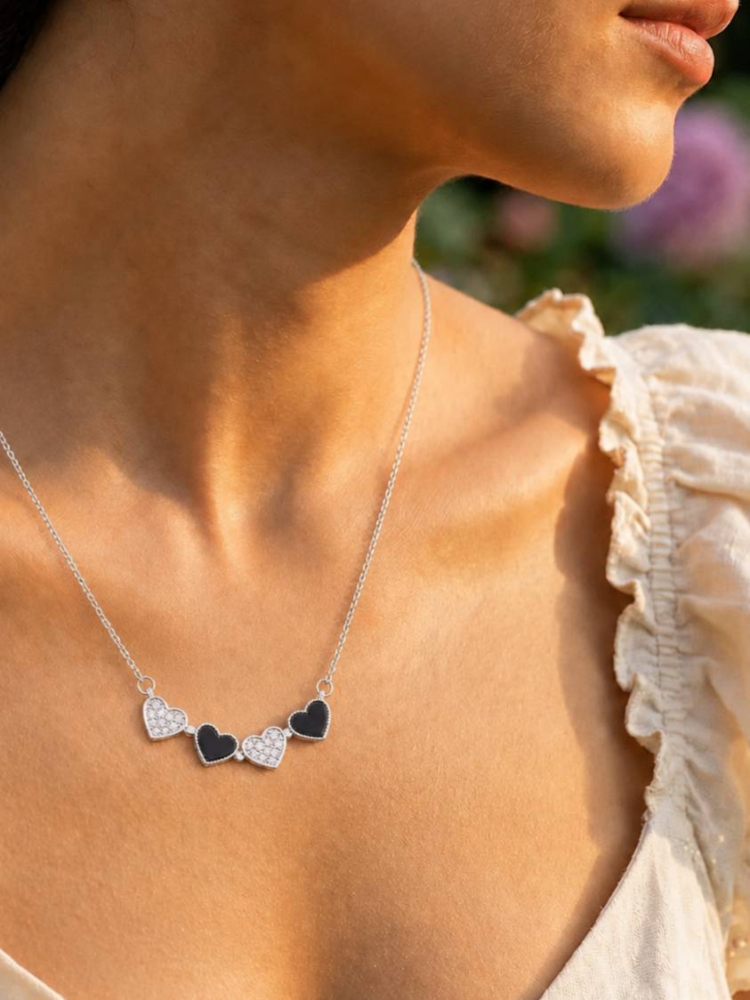 Bar necklace style with four alternating black enamel and CZ heart charms spread along the chain, worn at collarbone length