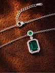 Close-up of emerald green CZ pendant necklace laid flat on a rust-brown textured surface showing lobster clasp