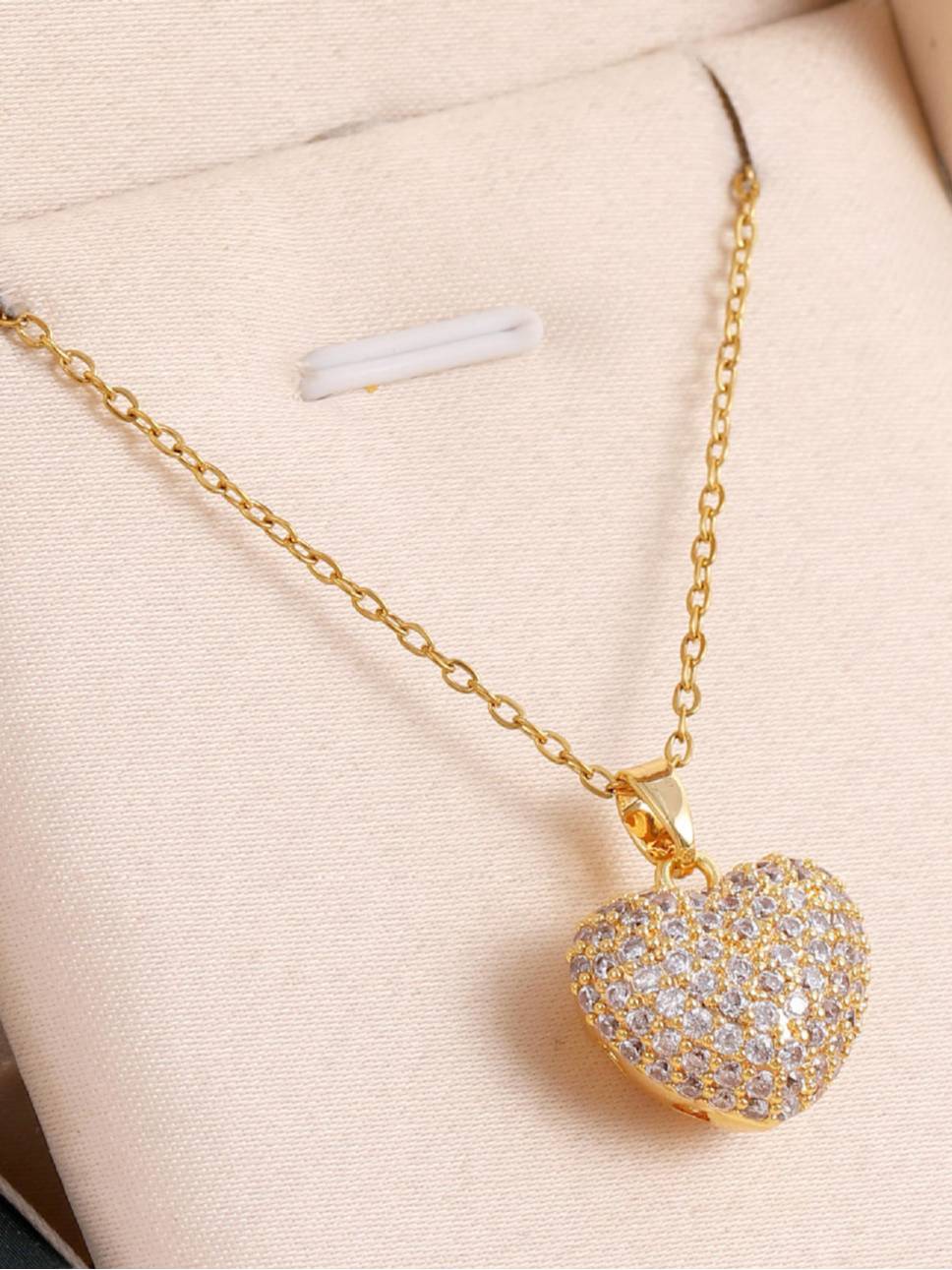 Gold-plated pave crystal heart pendant necklace laid flat on a cream jewellery box