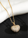 Puffy gold heart pendant with cubic zirconia stones on a cable chain against marble and black surface