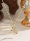 Close-up of gold-plated heart pendant with shell inlay and pave CZ detail resting on a neutral surface near amber glass decor