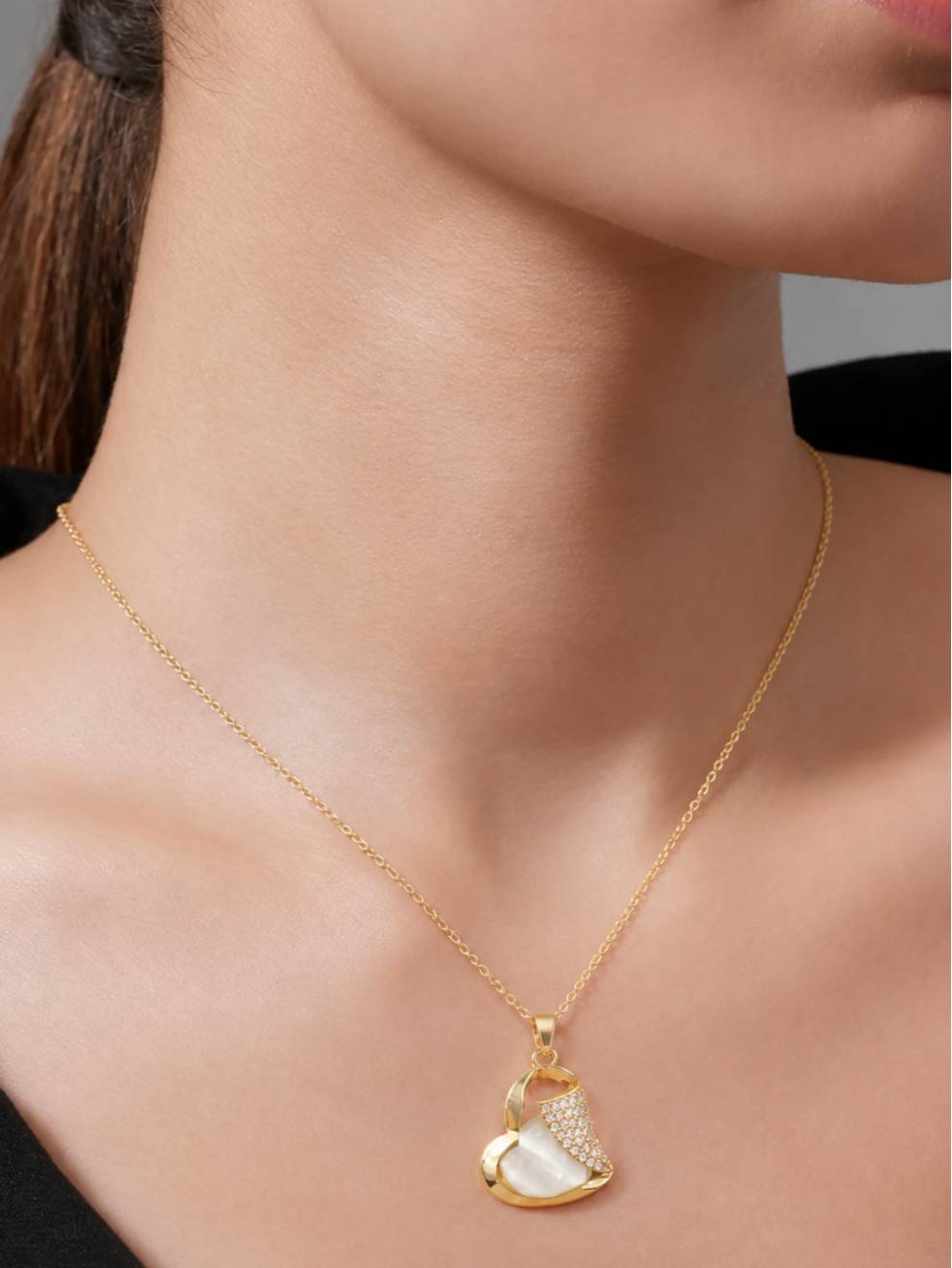Woman wearing gold-plated heart pendant necklace on a fine cable chain over a black top, shown at collarbone level