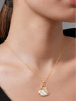 Woman wearing gold-plated heart pendant necklace on a fine cable chain over a black top, shown at collarbone level