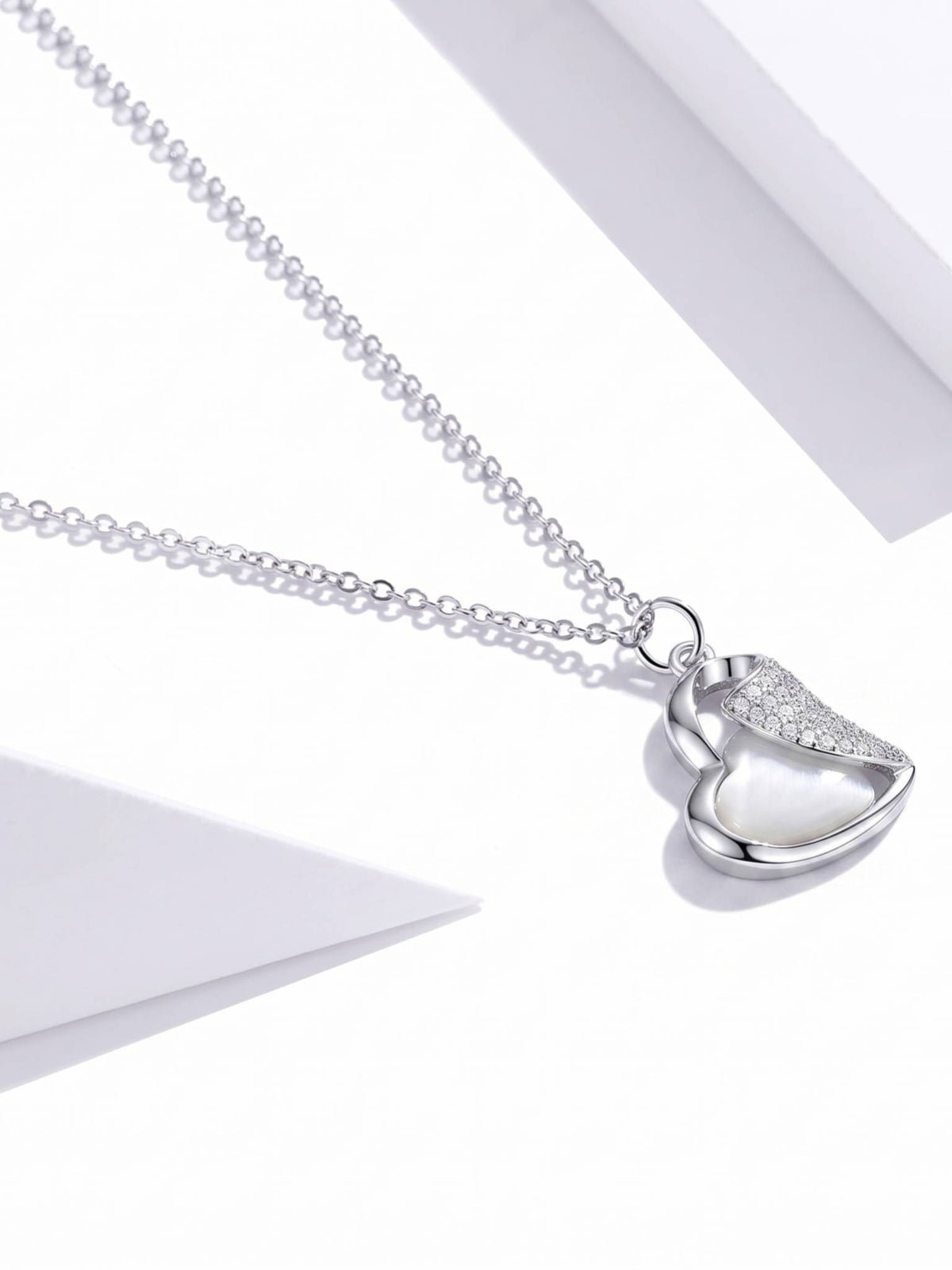 Close-up side angle of heart pendant necklace revealing texture and cable chain detail on white surface