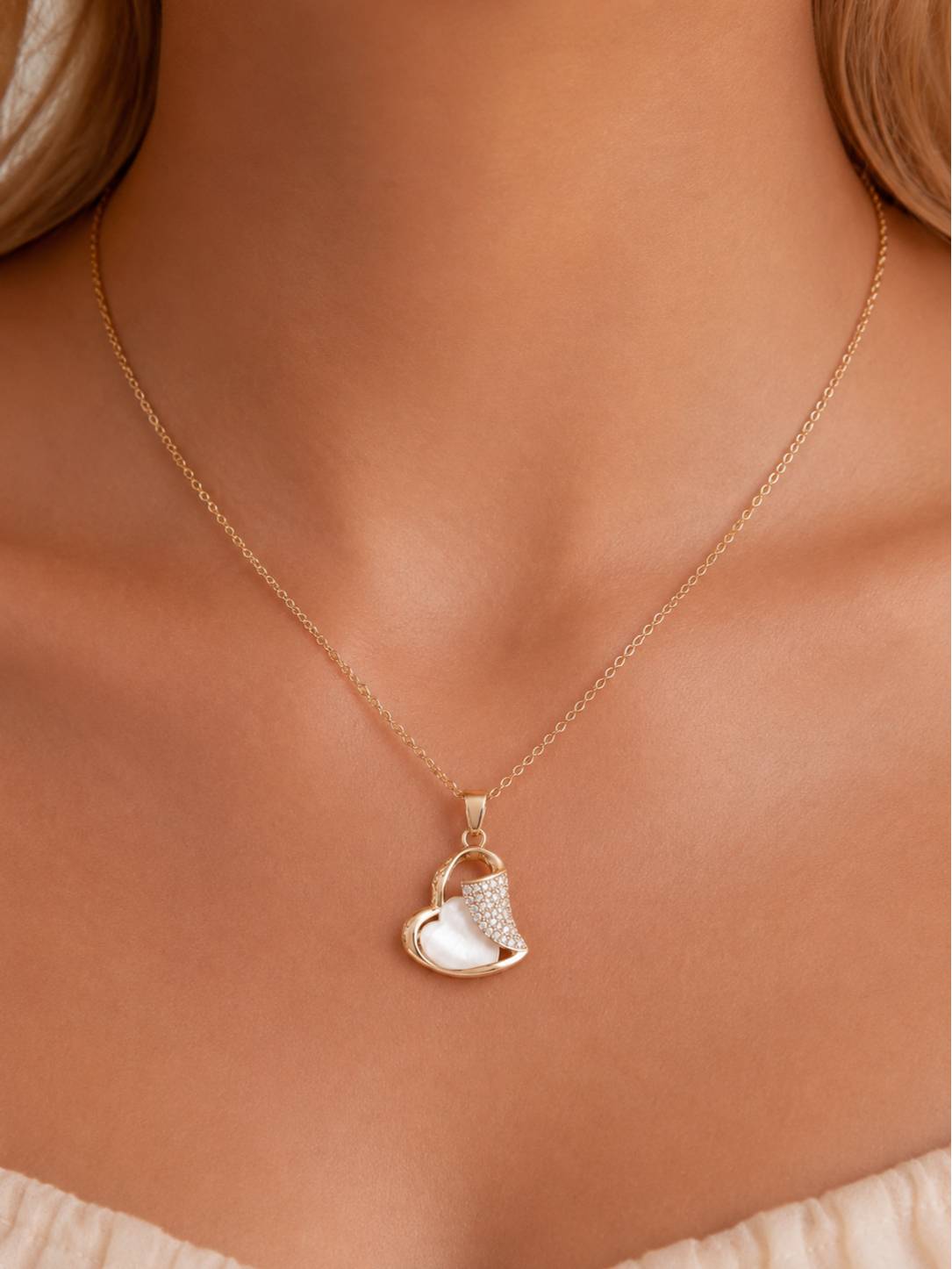 Rose gold heart pendant necklace worn on a model's neckline over a white top