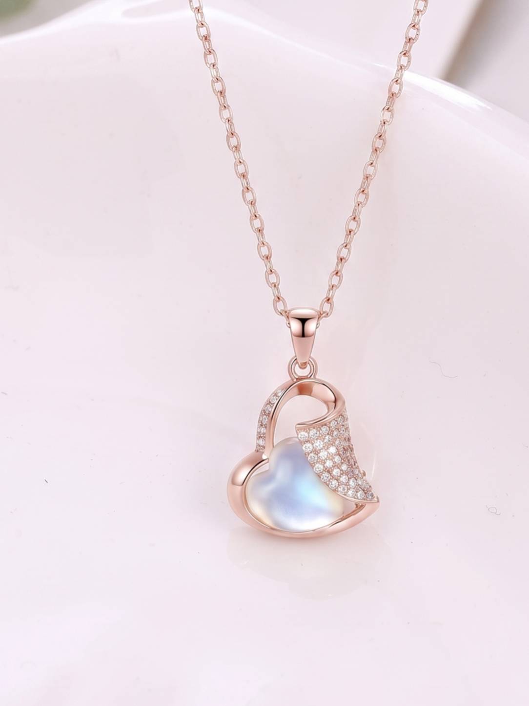 Close-up of rose gold heart pendant with moonstone and cubic zirconia on white surface