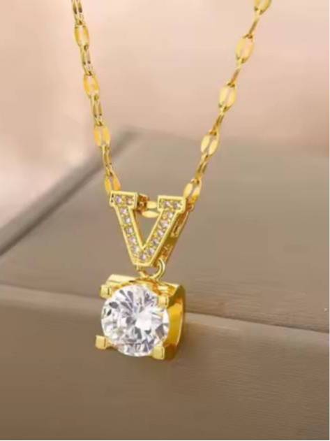 Gold V pendant necklace with pavé bail and solitaire stone shown against a beige fabric background