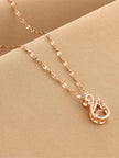 Close-up of rose gold swan pendant with zirconia stones on a textured beige surface