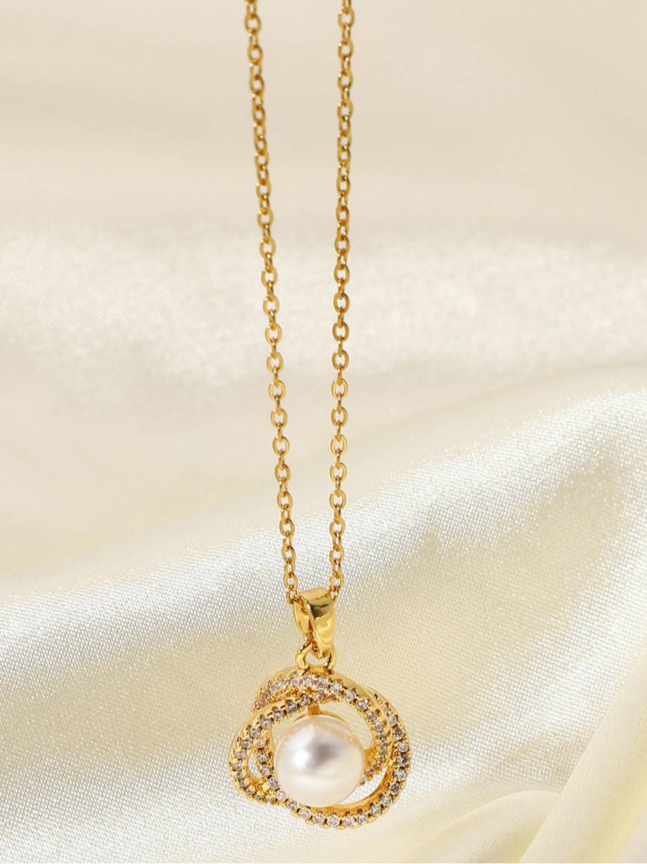 Gold-plated pearl pendant necklace with CZ-studded orbital rings hanging against cream fabric