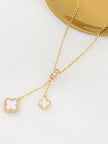 Side-angle view of double clover necklace on white surface beside a gold tray, highlighting charm size difference