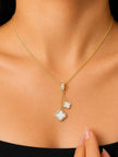 Model wearing gold-plated double clover pendant necklace against a black top, showing how it sits on the neckline