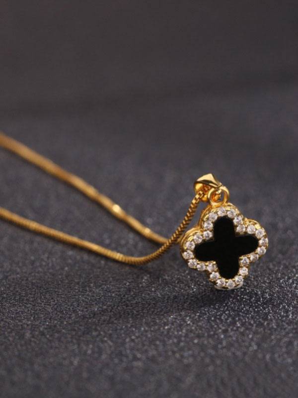 Close-up of gold-plated clover pendant with black enamel inlay and crystal border on a slim box chain against dark background
