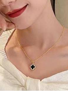Woman wearing gold-plated black enamel clover pendant necklace over a white off-shoulder top