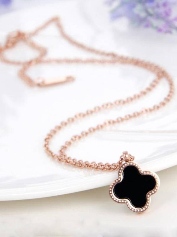 Rose gold clover pendant necklace with black inlay resting on a white ceramic plate
