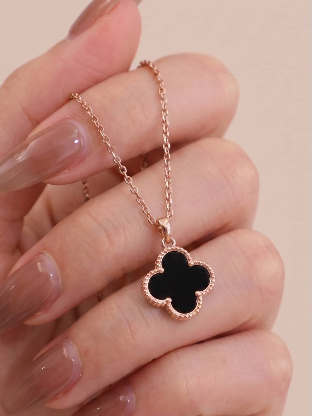 Close-up of black clover pendant necklace held between fingers showing milgrain beaded border