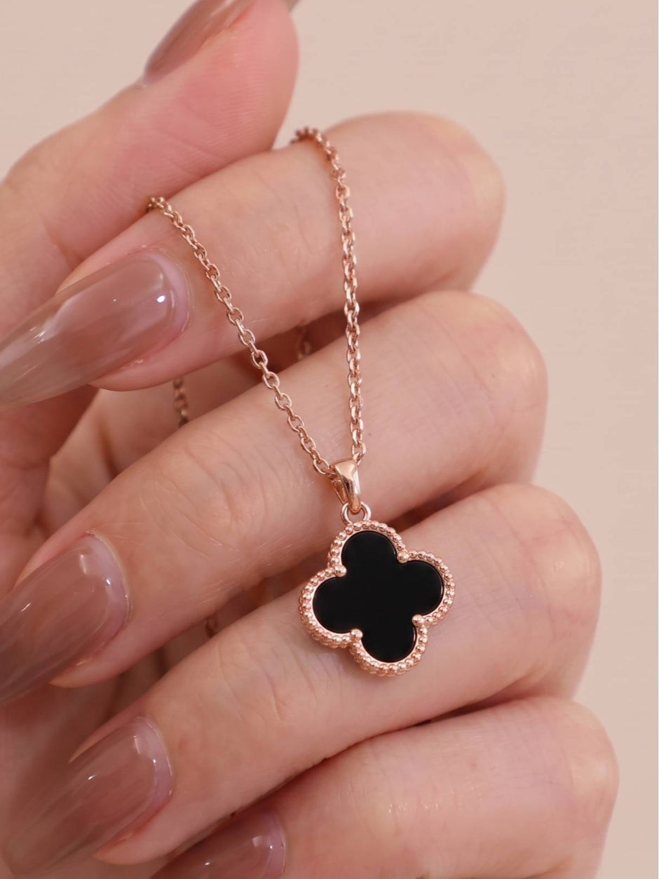 Close-up of black clover pendant necklace held between fingers showing milgrain beaded border
