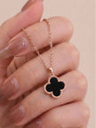 Close-up of black clover pendant necklace held between fingers showing milgrain beaded border