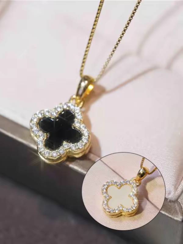 Close-up of black enamel four-leaf clover pendant with cubic zirconia border on gold chain, with white shell reverse variant shown in inset