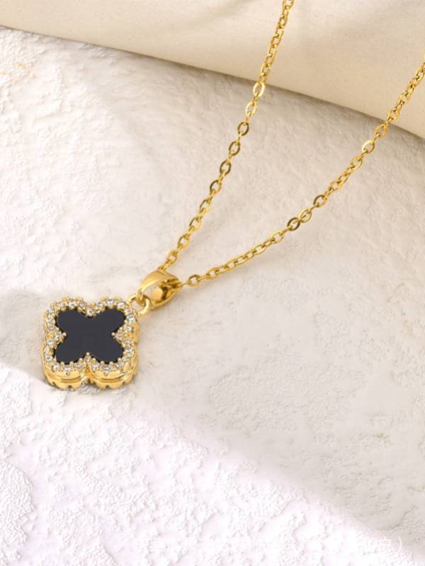 Black clover CZ pendant necklace displayed on textured white marble surface showing pendant detail and gold cable chain