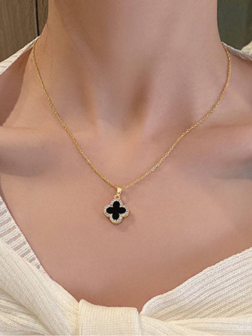 Woman wearing gold-plated black clover pendant necklace at collarbone length over white ribbed top
