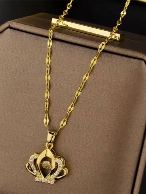 Gold-plated crown pendant necklace displayed in an open jewellery box on brown velvet