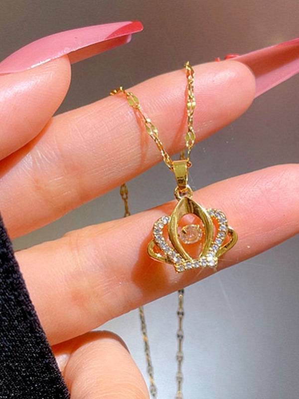 Close-up of gold-plated crown pendant with cubic zirconia held between fingers with pink nails