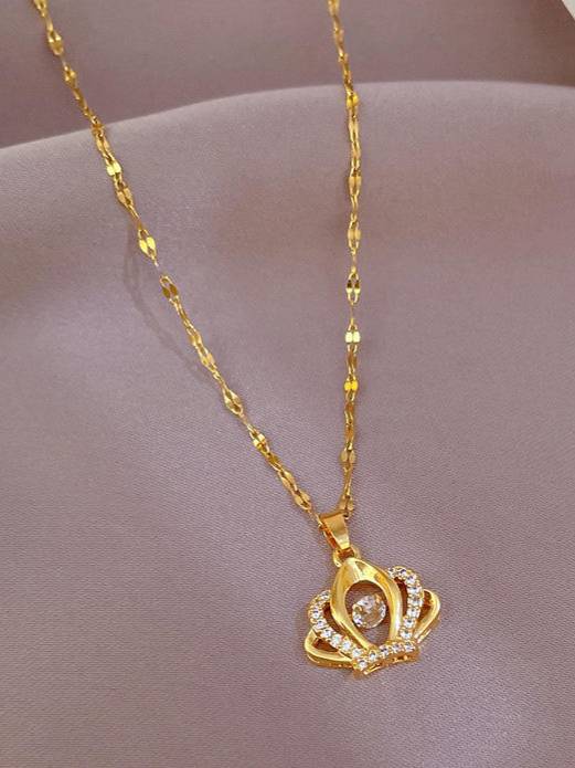 Gold-plated crown pendant necklace laid flat on a pink satin fabric surface