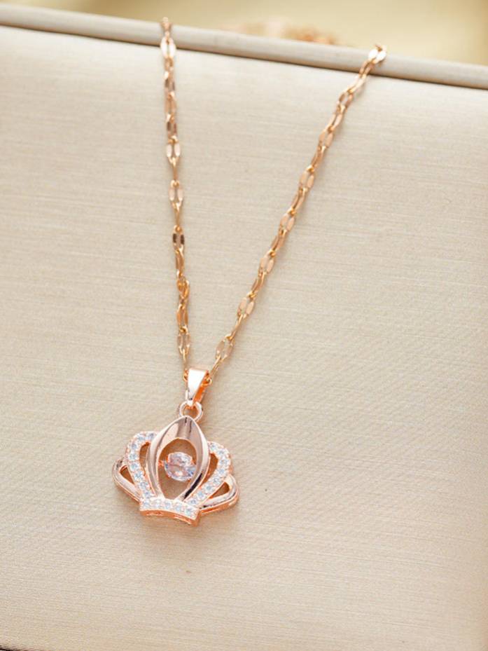 Rose gold crown pendant necklace with cubic zirconia border and centre stone laid flat on beige surface