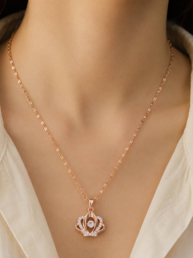 Rose gold crown pendant necklace worn on a woman's neck over a cream open-collar top