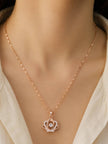 Rose gold crown pendant necklace worn on a woman's neck over a cream open-collar top