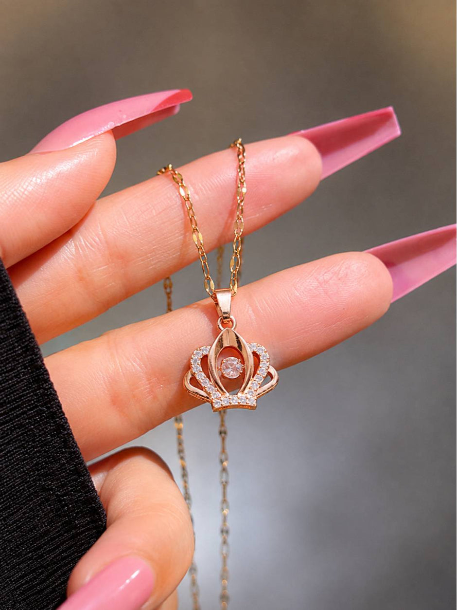 Rose gold crown pendant necklace held between fingers with long pink nails showing scale and detailing