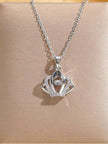Silver crown pendant necklace with pavé crystals and floating centre stone laid on a beige display surface