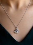 Silver crown pendant necklace worn around a woman's neck over a dark teal v-neck top