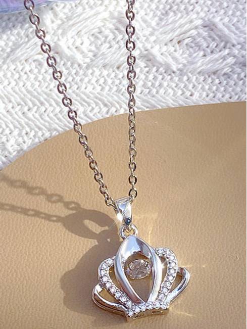 Crown pendant necklace with cubic zirconia detailing resting on a gold surface beside a white fabric