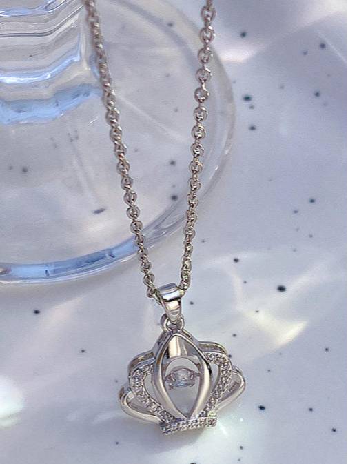 Silver crown pendant necklace with fine cable chain laid on a white surface near a glass dish
