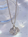 Silver crown pendant necklace with fine cable chain laid on a white surface near a glass dish