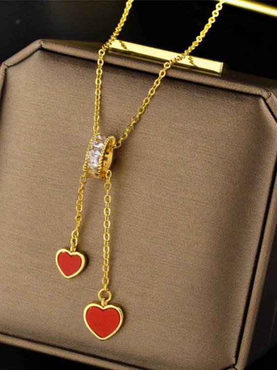 Gold-plated lariat necklace with two red enamel heart charms displayed on a brown jewellery box