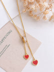 Gold lariat necklace with dual red heart pendants and crystal barrel slider laid flat on linen pouch with dried flowers