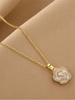 Close-up of gold-plated rose flower pendant with cubic zirconia stones on a beige fabric surface