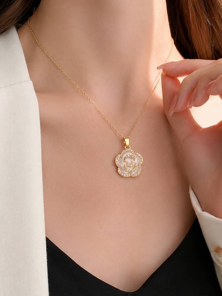 Woman wearing gold-plated shell flower pendant necklace over a black top with white blazer