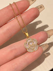 Gold-plated shell flower pendant necklace held between fingers showing scale and cubic zirconia detail