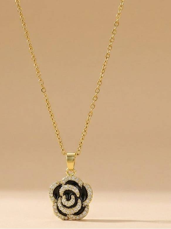 Full view of gold-tone chain with black enamel floral pendant against a soft beige background