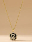 Full view of gold-tone chain with black enamel floral pendant against a soft beige background