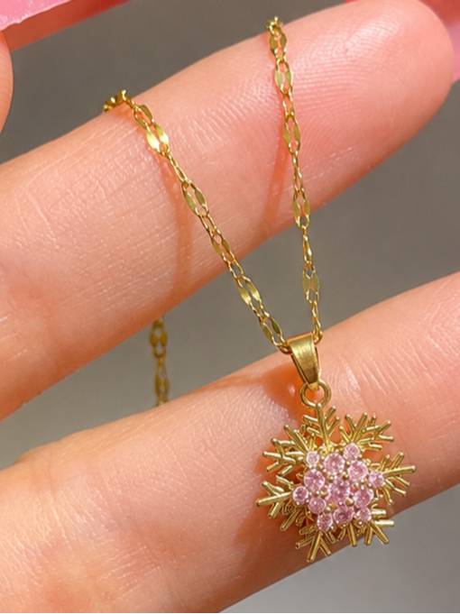 Close-up of gold snowflake pendant with pink CZ cluster held between two fingers showing fine detail