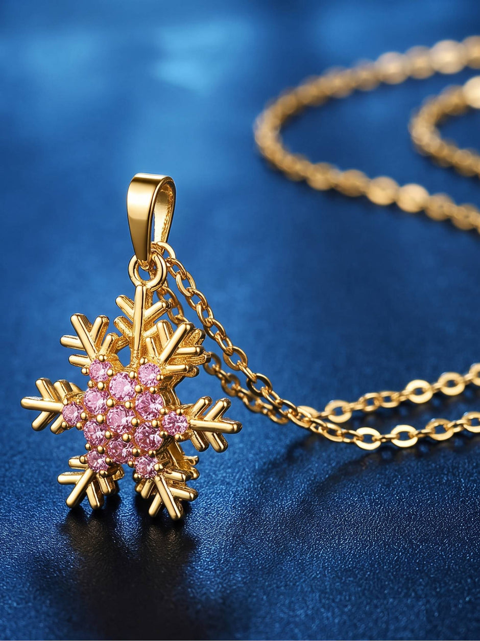 Gold snowflake pendant with pink zirconia stones resting on a dark blue surface with chain in background