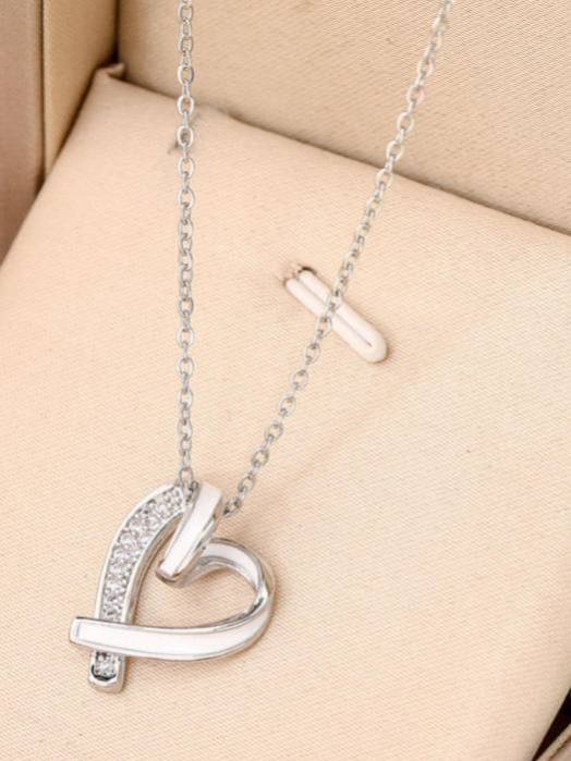 Silver open-heart pendant necklace with cubic zirconia stones displayed in a beige jewellery box alongside a small cross charm