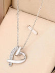 Silver open-heart pendant necklace with cubic zirconia stones displayed in a beige jewellery box alongside a small cross charm