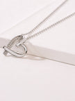 Close-up of rhodium-plated heart pendant with pavé CZ arch resting on a white surface, showing twisted ribbon detail